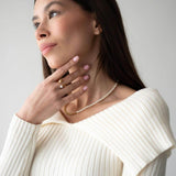 Жена с хибридно колие от перли и синджир, облечена в бяла блуза, позираща на неутрален фон.