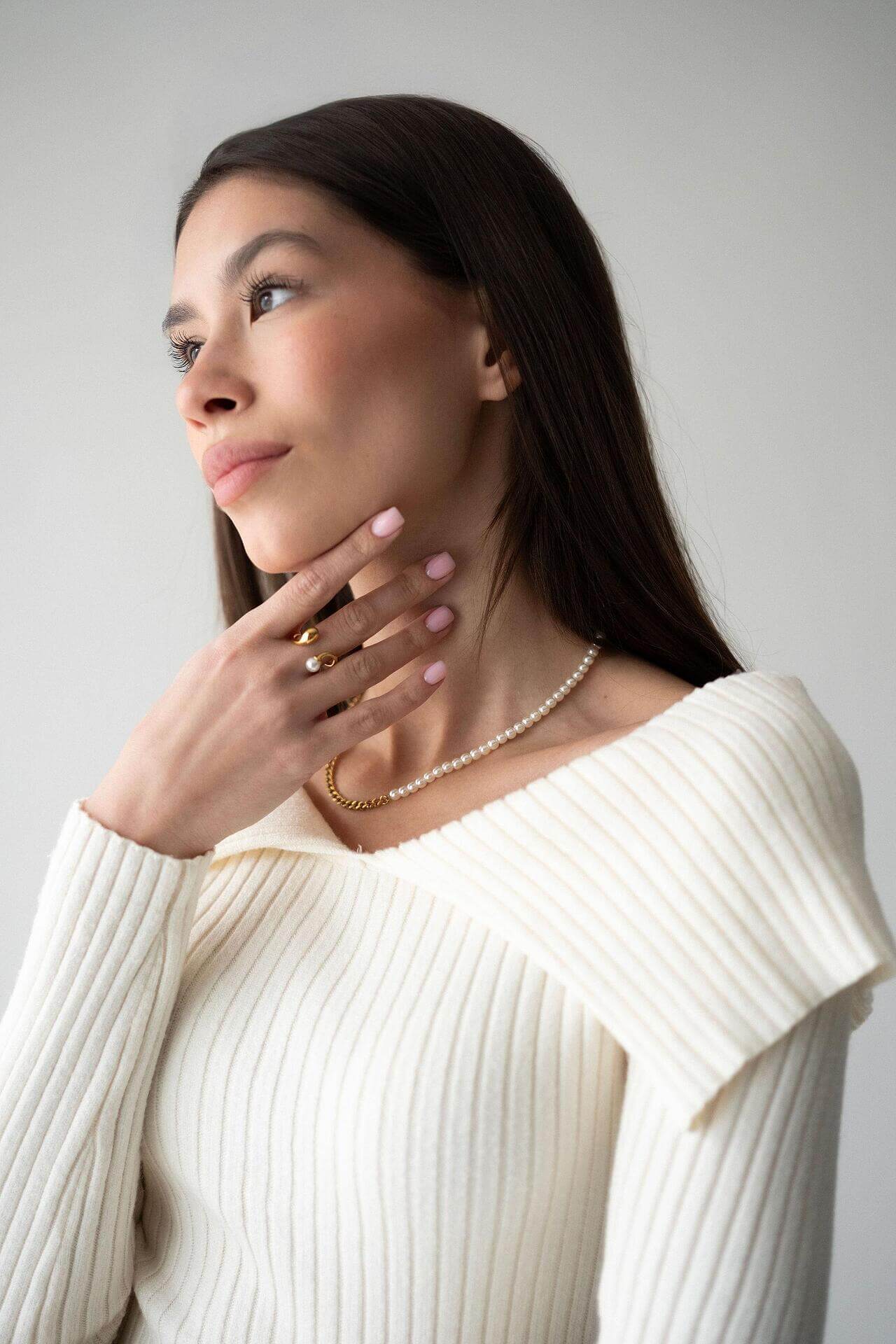 Жена с хибридно колие от перли и синджир, облечена в бяла блуза, позираща на неутрален фон.