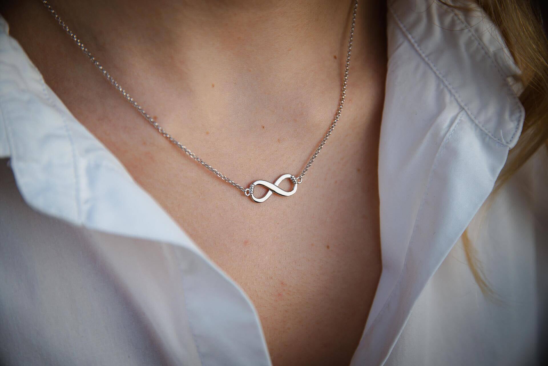 Сребърно елегантно колие безкрайност S925 на нежна дама, носеща бял риза, символизираща вечна любов.