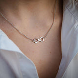 Сребърно елегантно колие безкрайност S925 на нежна дама, носеща бял риза, символизираща вечна любов.