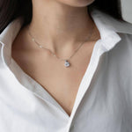 Сребърно колие S925 с цирконов камък, носено върху бяла риза, близък план на шията.